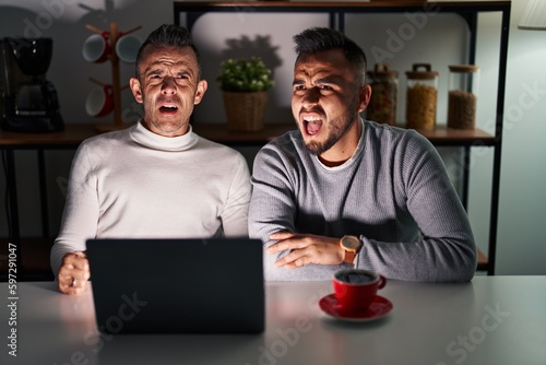 Homosexual couple using computer laptop angry and mad screaming frustrated and furious, shouting with anger. rage and aggressive concept.