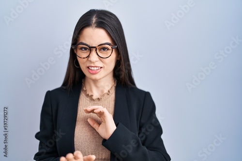 Young brunette woman standing over blue background disgusted expression, displeased and fearful doing disgust face because aversion reaction. with hands raised