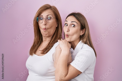 Hispanic mother and daughter wearing casual white t shirt making fish face with mouth and squinting eyes, crazy and comical.
