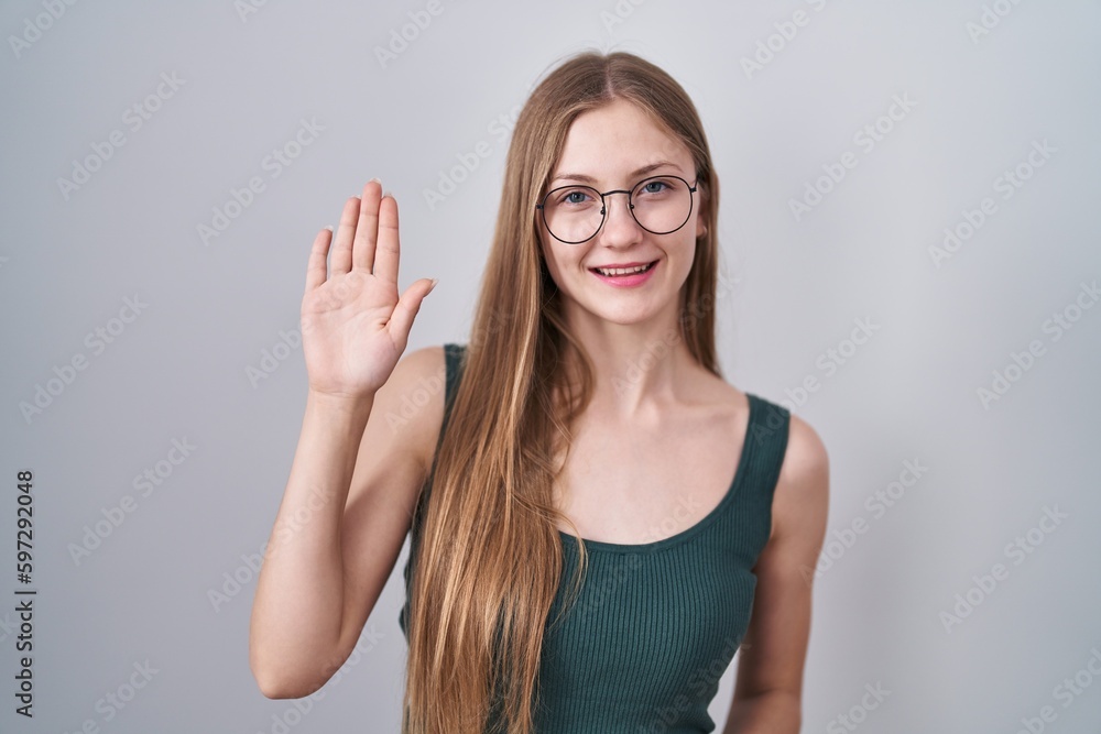 Young caucasian woman standing over white background waiving saying hello happy and smiling, friendly welcome gesture Young caucasian woman standing over white background waiving saying hello happy and smiling, friendly welcome gesture