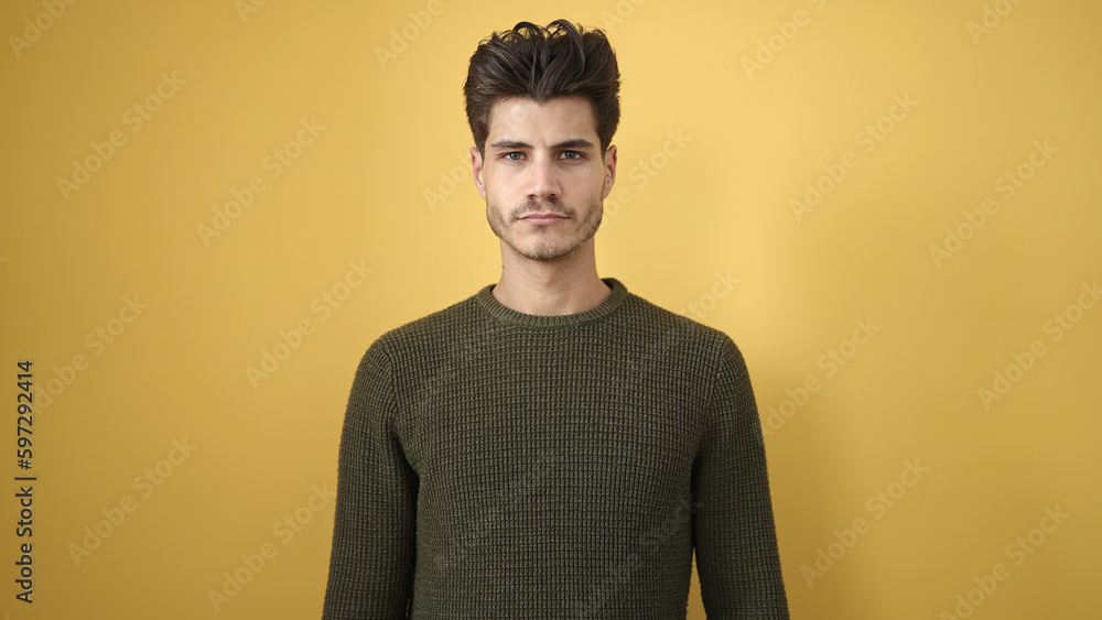 Young hispanic man standing with serious expression over isolated yellow background Young hispanic man standing with serious expression over isolated yellow background