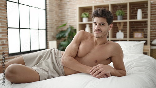 Young hispanic man smiling confident lying on bed at bedroom