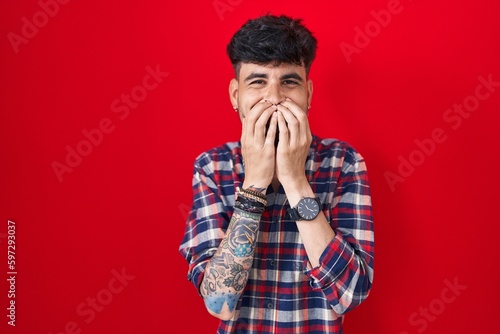 Принти на полотні Young hispanic man with beard standing over red background laughing and embarras