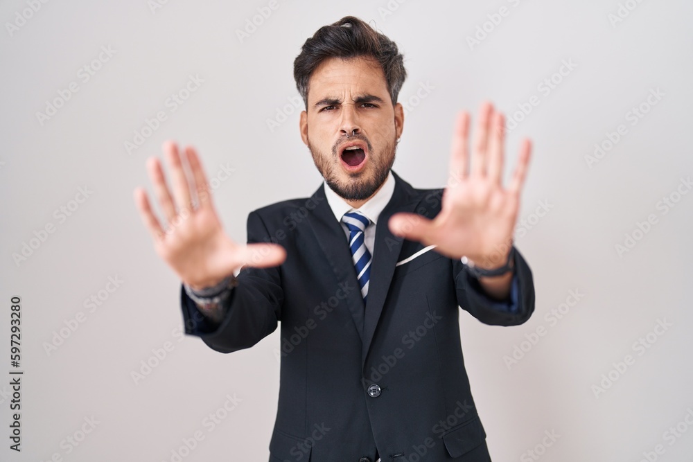 Young hispanic man with tattoos wearing business suit and tie doing stop gesture with hands palms, angry and frustration expression Young hispanic man with tattoos wearing business suit and tie doing stop gesture with hands palms, angry and frustration expression