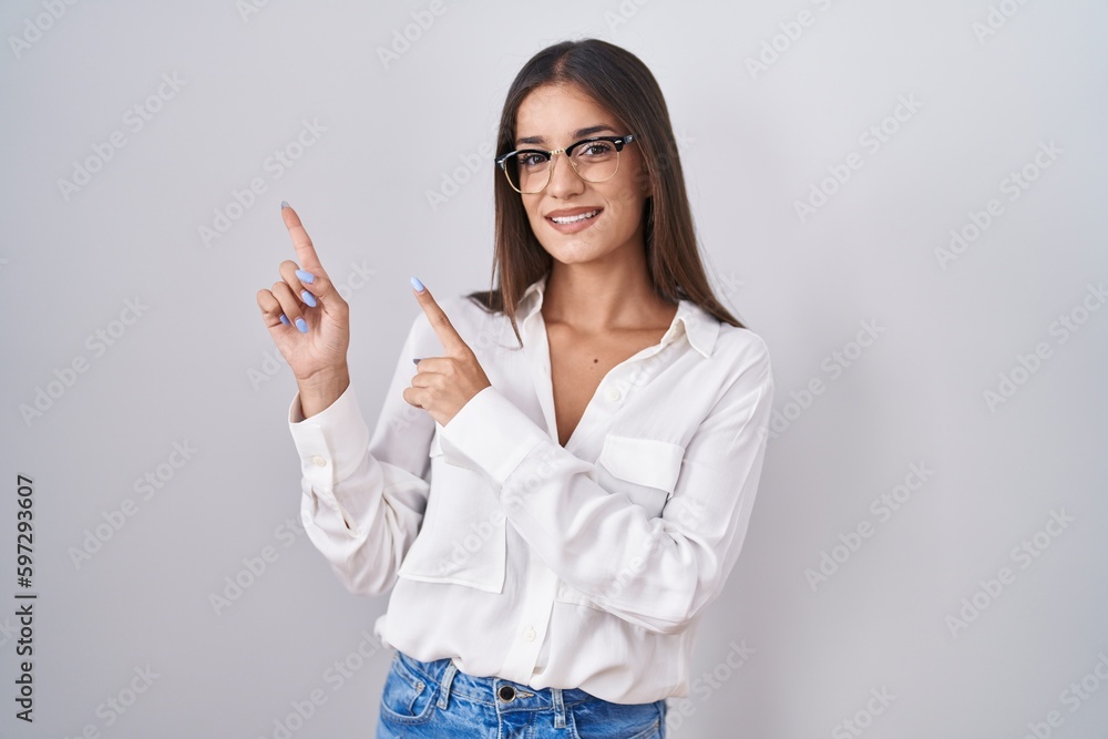 Young brunette woman wearing glasses smiling and looking at the camera pointing with two hands and fingers to the side. Young brunette woman wearing glasses smiling and looking at the camera pointing with two hands and fingers to the side.
