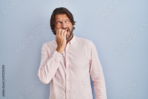 Handsome middle age man wearing elegant shirt background looking stressed and nervous with hands on mouth biting nails. anxiety problem.