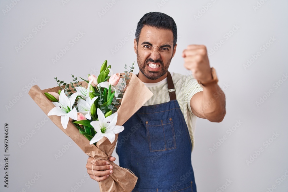 Hispanic man with beard working as florist angry and mad raising fist frustrated and furious while shouting with anger. rage and aggressive concept. Hispanic man with beard working as florist angry and mad raising fist frustrated and furious while shouting with anger. rage and aggressive concept.