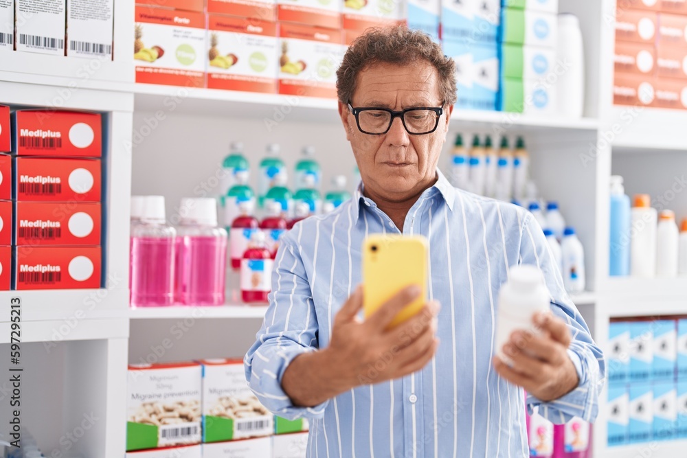 Middle age man customer using smartphone holding pills bottle at pharmacy