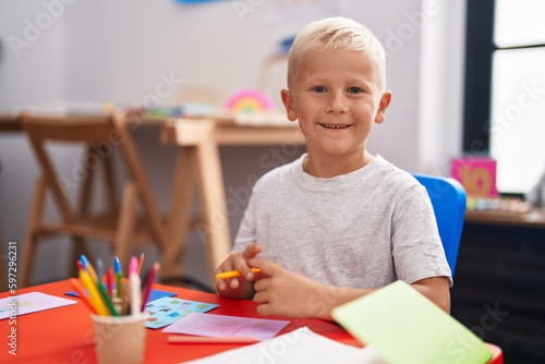 Little caucasian boy painting at the school looking positive and happy standing and smiling with a confident smile showing teeth