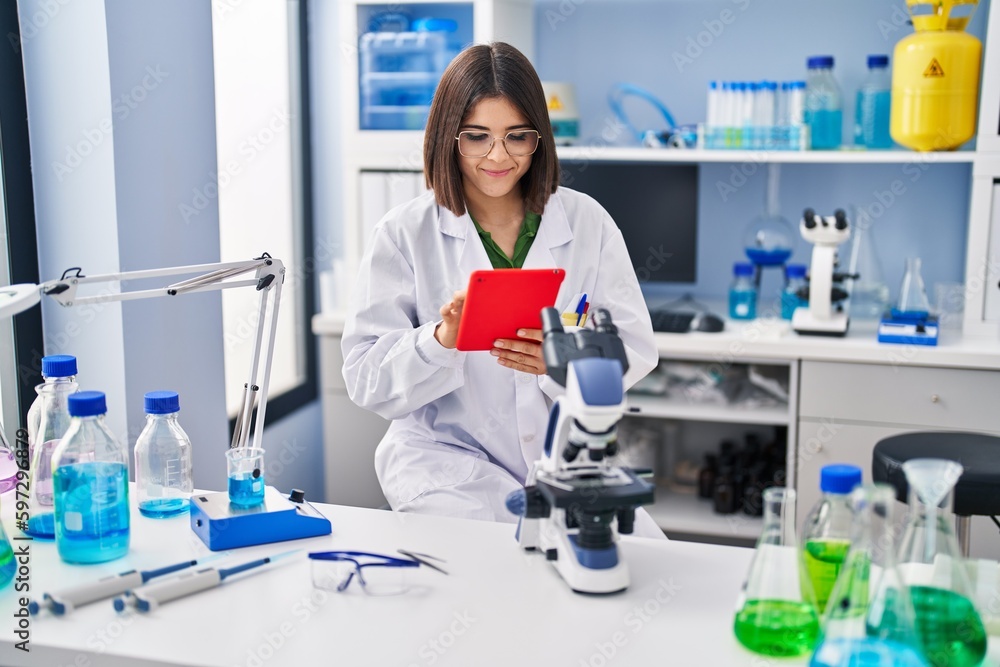 Young beautiful hispanic woman scientist smiling confident using touchpad at laboratory Young beautiful hispanic woman scientist smiling confident using touchpad at laboratory