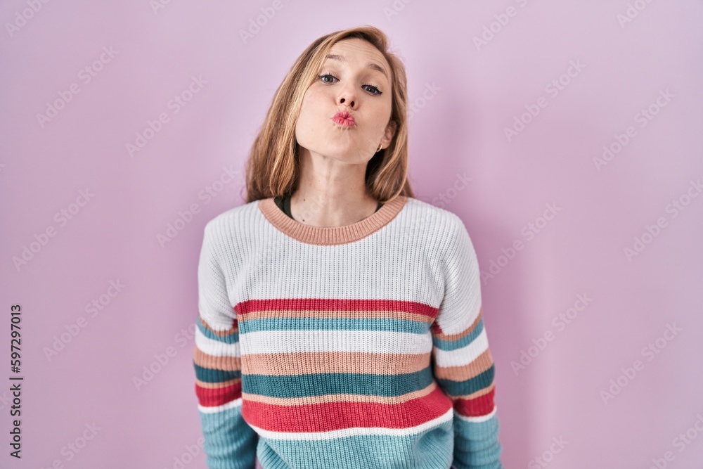 Young blonde woman standing over pink background looking at the camera blowing a kiss on air being lovely and sexy. love expression. Young blonde woman standing over pink background looking at the camera blowing a kiss on air being lovely and sexy. love expression.