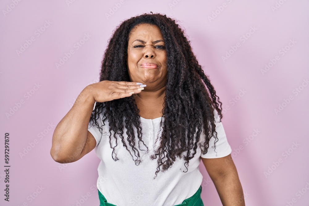 Plus size hispanic woman standing over pink background cutting throat with hand as knife, threaten aggression with furious violence