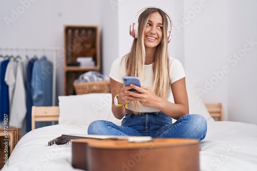 Young beautiful hispanic woman listening to music sitting on bed at bedroom