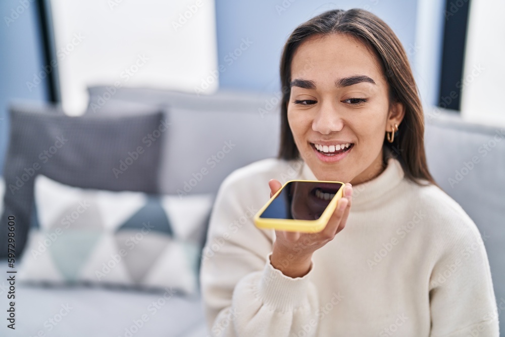 Young hispanic woman talking on the smartphone sitting on sofa at home