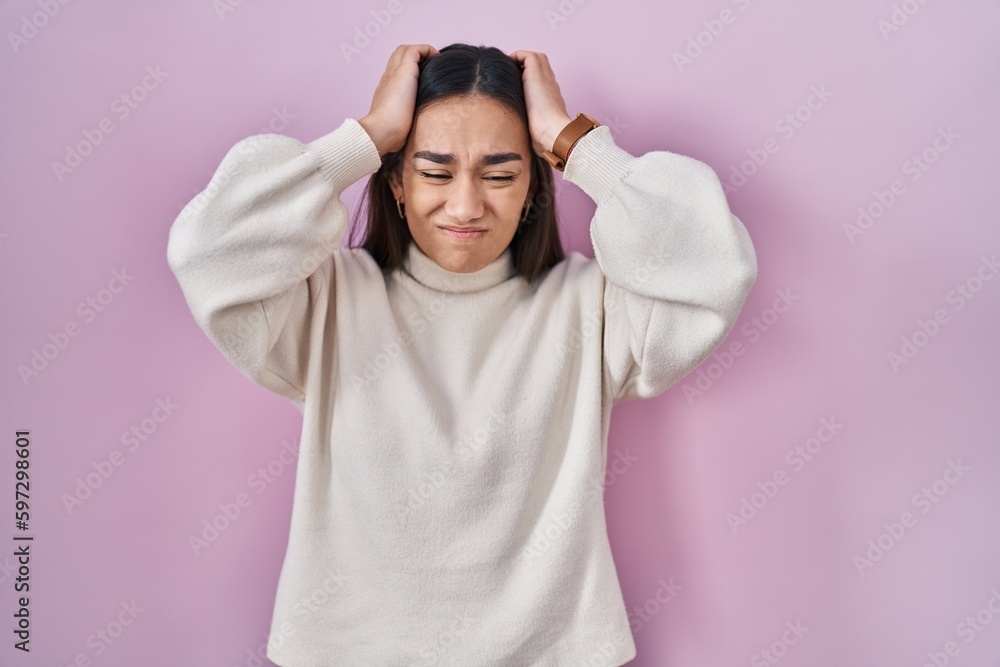Young south asian woman standing over pink background suffering from headache desperate and stressed because pain and migraine. hands on head. Young south asian woman standing over pink background suffering from headache desperate and stressed because pain and migraine. hands on head.