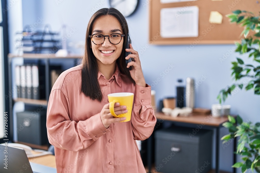 Young hispanic woman business worker talking on smartphone drinking coffee at office Young hispanic woman business worker talking on smartphone drinking coffee at office