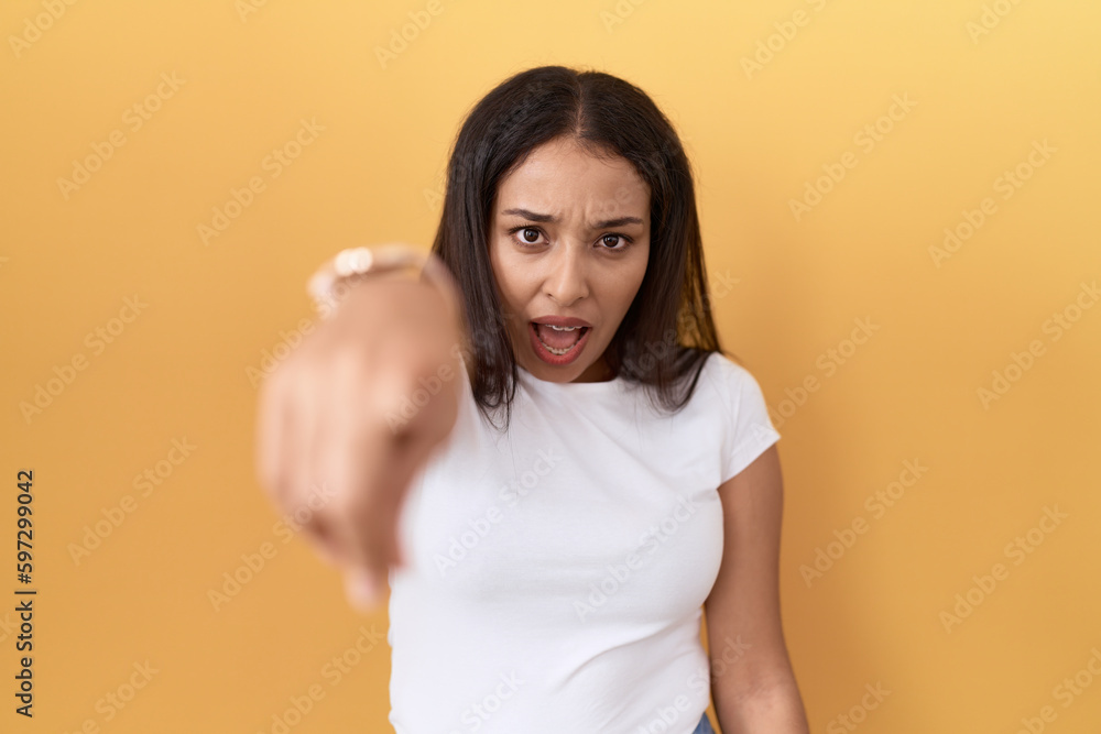 Young arab woman wearing casual white t shirt over yellow background pointing displeased and frustrated to the camera, angry and furious with you Young arab woman wearing casual white t shirt over yellow background pointing displeased and frustrated to the camera, angry and furious with you