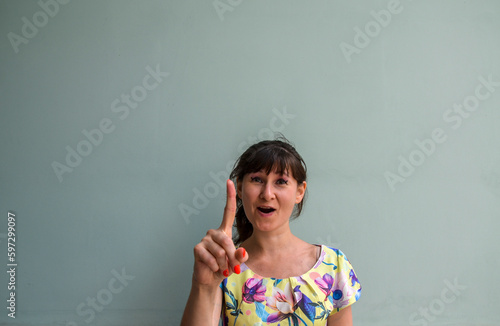 Funny cheerful young woman holding finger up having idea and posing on gray background
