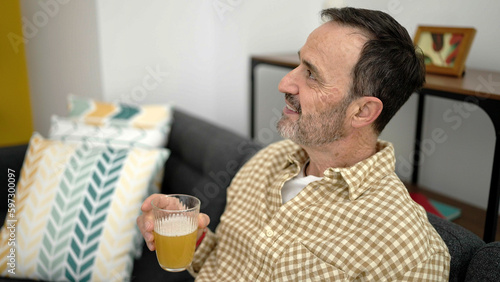 Middle age man holding glass of beer sitting on sofa at home