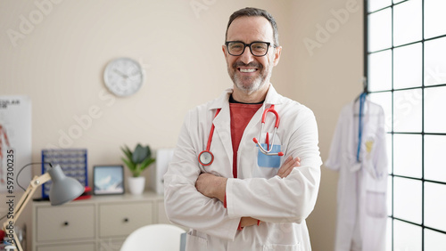 Middle age man doctor smiling confident standing with arms crossed gesture at clinic