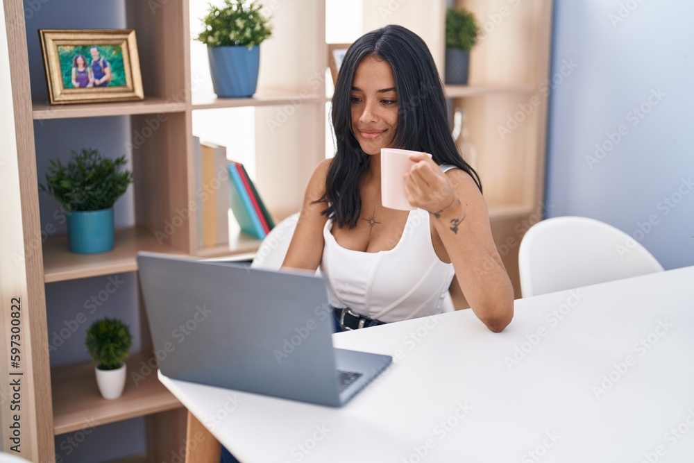 Young hispanic woman using laptop drinking coffee at home Young hispanic woman using laptop drinking coffee at home