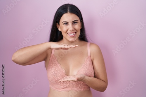 Young hispanic woman wearing pink bra gesturing with hands showing big and large size sign, measure symbol. smiling looking at the camera. measuring concept.