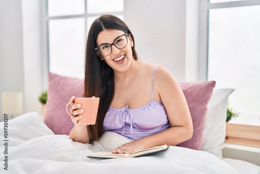Young hispanic woman drinking cup of coffee reading book at bedroom Young hispanic woman drinking cup of coffee reading book at bedroom