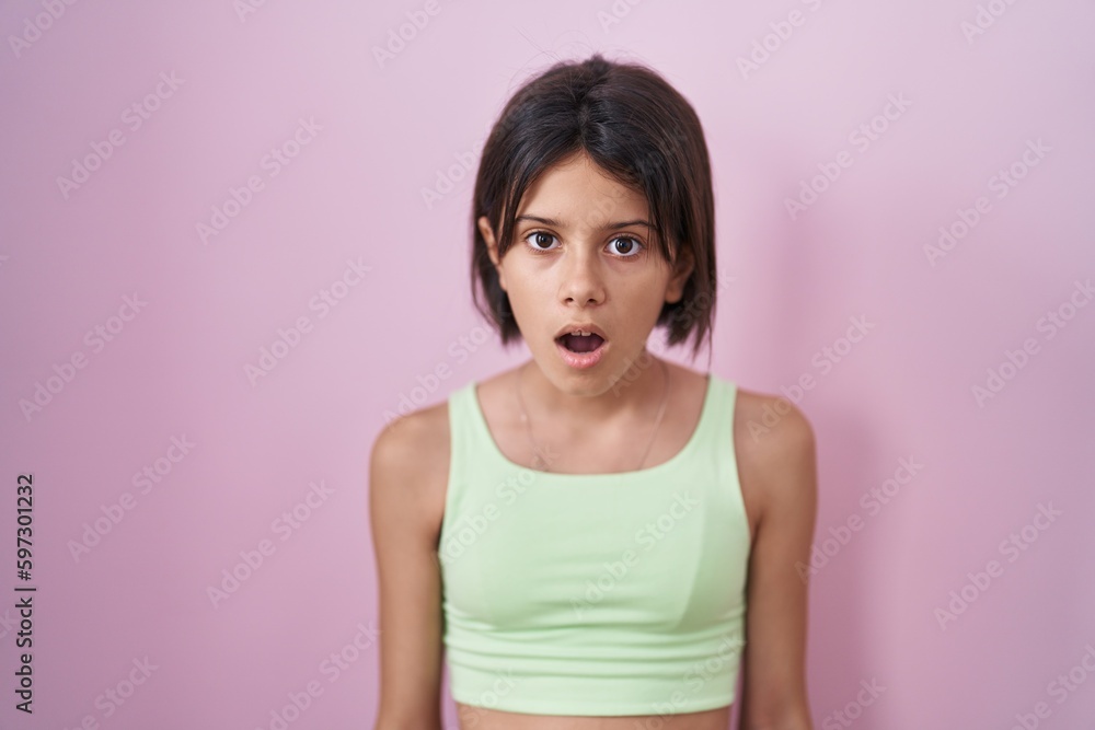 Young girl standing over pink background in shock face, looking skeptical and sarcastic, surprised with open mouth Young girl standing over pink background in shock face, looking skeptical and sarcastic, surprised with open mouth