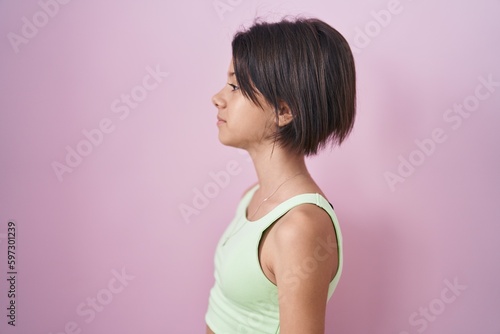 Young girl standing over pink background looking to side, relax profile pose with natural face and confident smile.