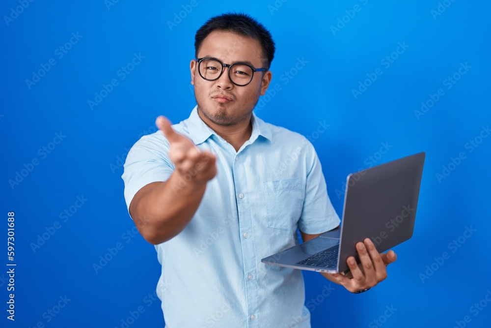 Chinese young man using computer laptop looking at the camera blowing a kiss with hand on air being lovely and sexy. love expression. Chinese young man using computer laptop looking at the camera blowing a kiss with hand on air being lovely and sexy. love expression.