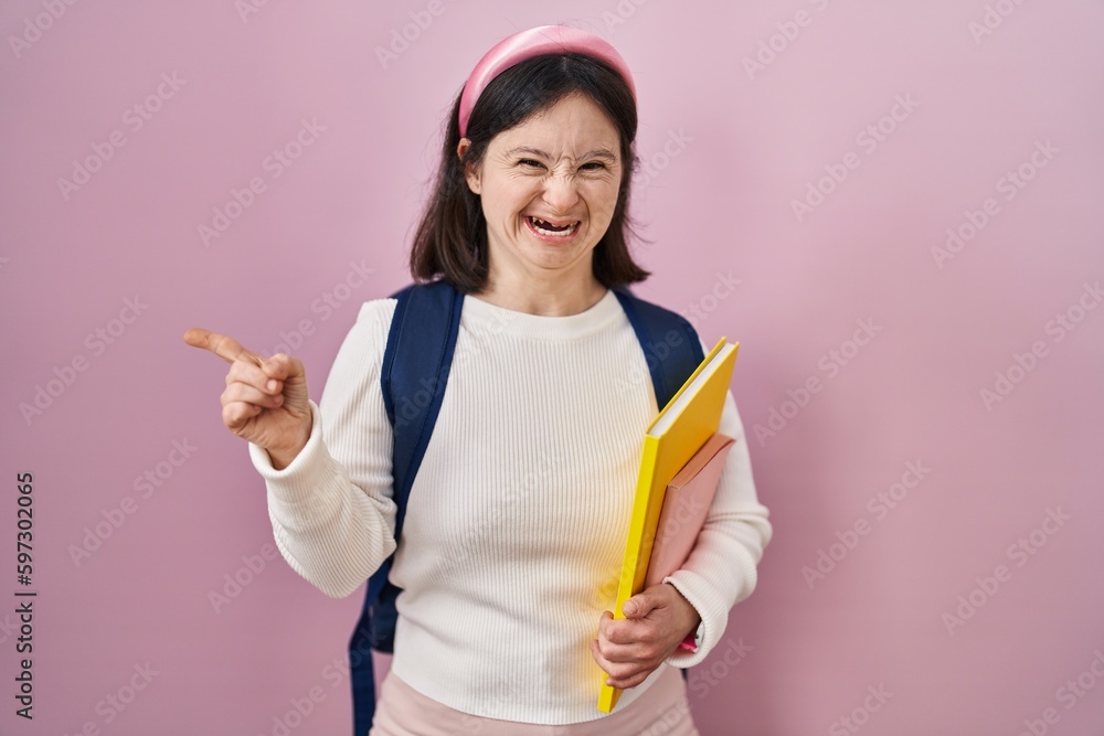 Woman with down syndrome wearing student backpack and holding books pointing aside worried and nervous with forefinger, concerned and surprised expression Woman with down syndrome wearing student backpack and holding books pointing aside worried and nervous with forefinger, concerned and surprised expression
