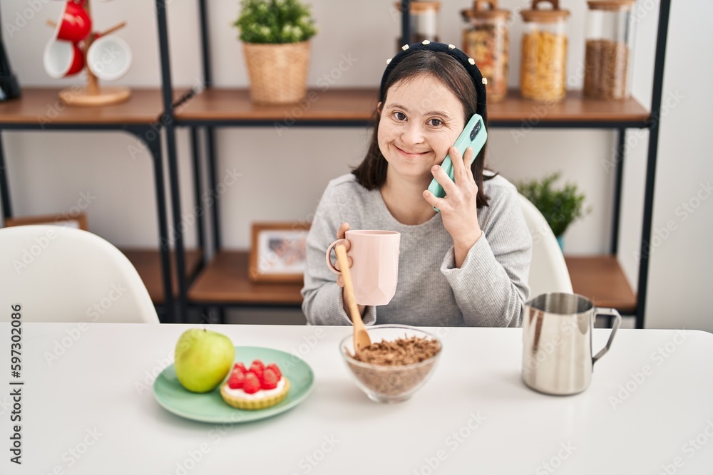 Young woman with down syndrome talking on the smartphone having breakfast at home Young woman with down syndrome talking on the smartphone having breakfast at home