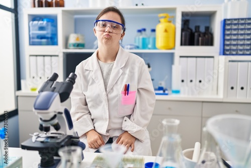 Hispanic girl with down syndrome working at scientist laboratory looking at the camera blowing a kiss on air being lovely and sexy. love expression.