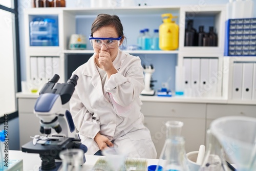 Hispanic girl with down syndrome working at scientist laboratory feeling unwell and coughing as symptom for cold or bronchitis. health care concept.