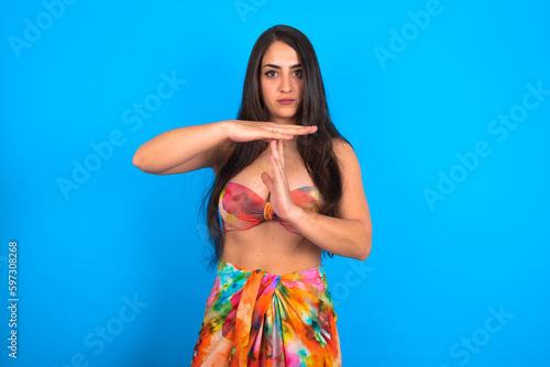 beautiful brunette woman wearing swimwear over blue background being upset showing a timeout gesture, needs stop, asks time for rest after hard work,