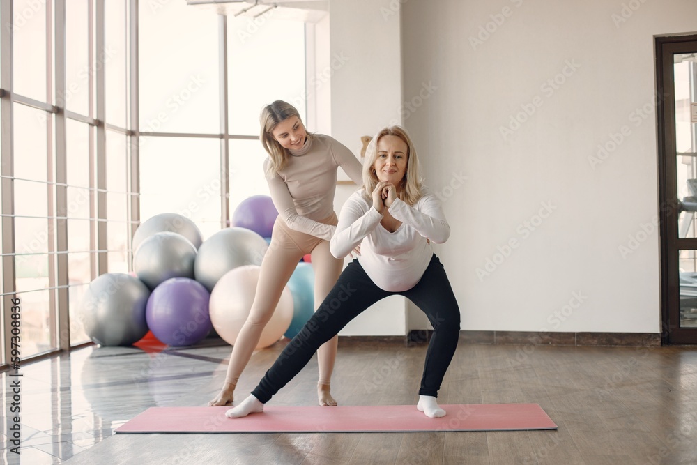 Obraz premium Trainer helping pregnant woman to do yoga asana