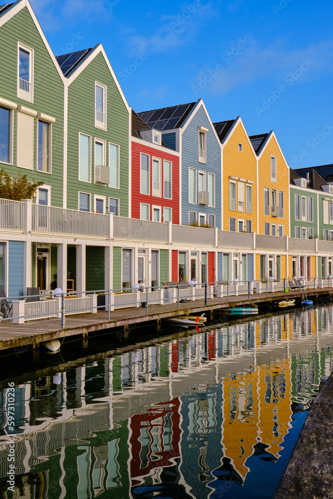 Houten, The Netherlands - April 25 2023. Row of colourful wooden lakeside houses. Reflected in the water of lake De Rietplas. Diminishing perspective.