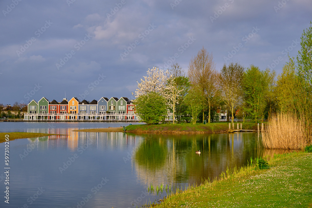Obraz premium Houten, The Netherlands - April 25 2023. Trees and colourful wooden lakeside houses reflected in the water of lake De Rietplas.