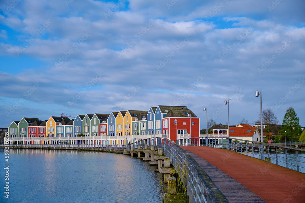 Houten, The Netherlands - April 25 2023. Wooden bridge alongside colourful wooden lakeside houses. Reflected in the water of lake De Rietplas.