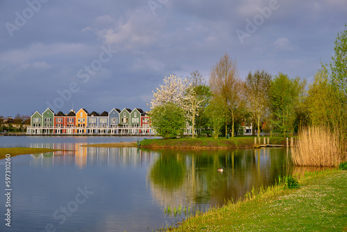 Houten, The Netherlands - April 25 2023. Trees and colourful wooden lakeside houses reflected in the water of lake De Rietplas.