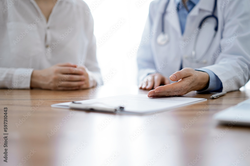 Doctor and patient discussing something while sitting near each other at the wooden desk in clinic. Medicine concept Doctor and patient discussing something while sitting near each other at the wooden desk in clinic. Medicine concept