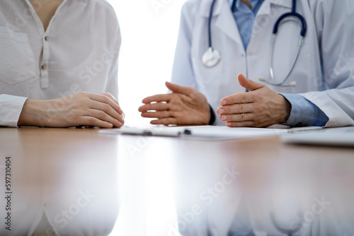 Doctor and patient discussing something while sitting near each other at the wooden desk in clinic. Medicine concept © rogerphoto