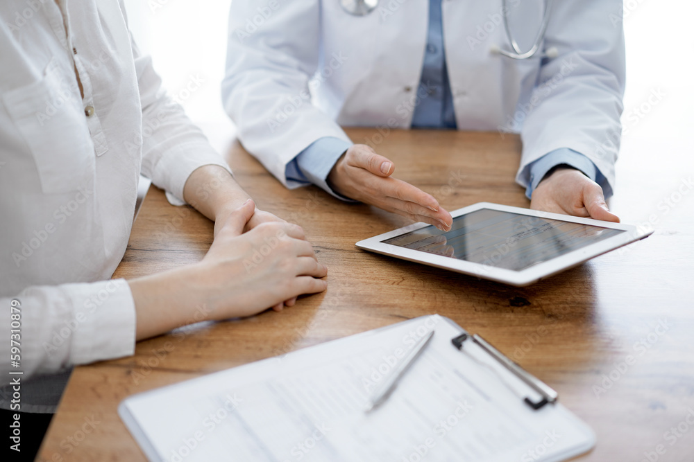 Doctor and patient sitting at the wooden desk in clinic. Female physician's hands pointing into laptop computer monitor, close up. Medicine concept Doctor and patient sitting at the wooden desk in clinic. Female physician's hands pointing into laptop computer monitor, close up. Medicine concept