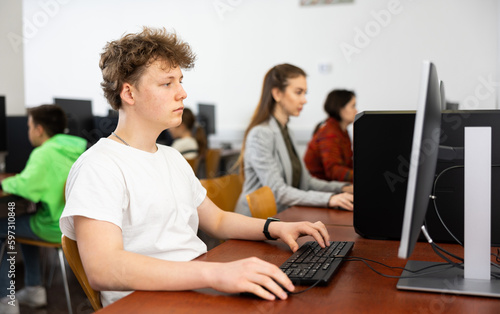Teenage boy sitting at table and using computer during lesson.