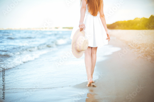 Young woman on a beach holding a white hat. Legs close up © rogerphoto