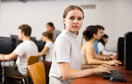 Teenage girl sitting at table and using computer during lesson.