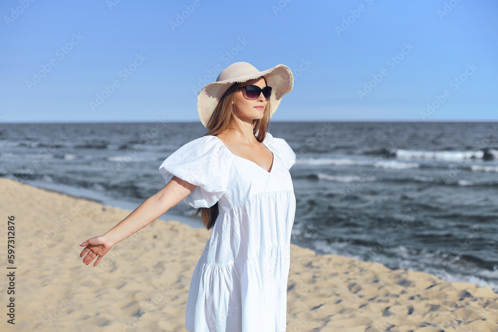 Happy blonde woman is on the ocean beach in a white dress and sunglasses, open arms