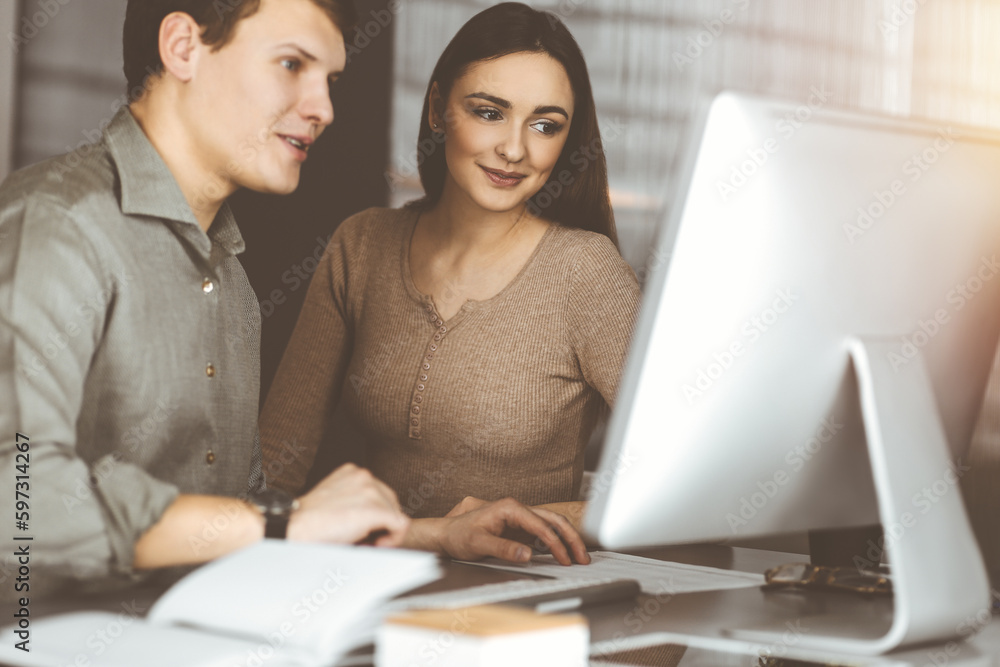 Friendly young businessman in a green shirt is working on computer, while sitting together at the desk with a female colleague in a modern office Friendly young businessman in a green shirt is working on computer, while sitting together at the desk with a female colleague in a modern office