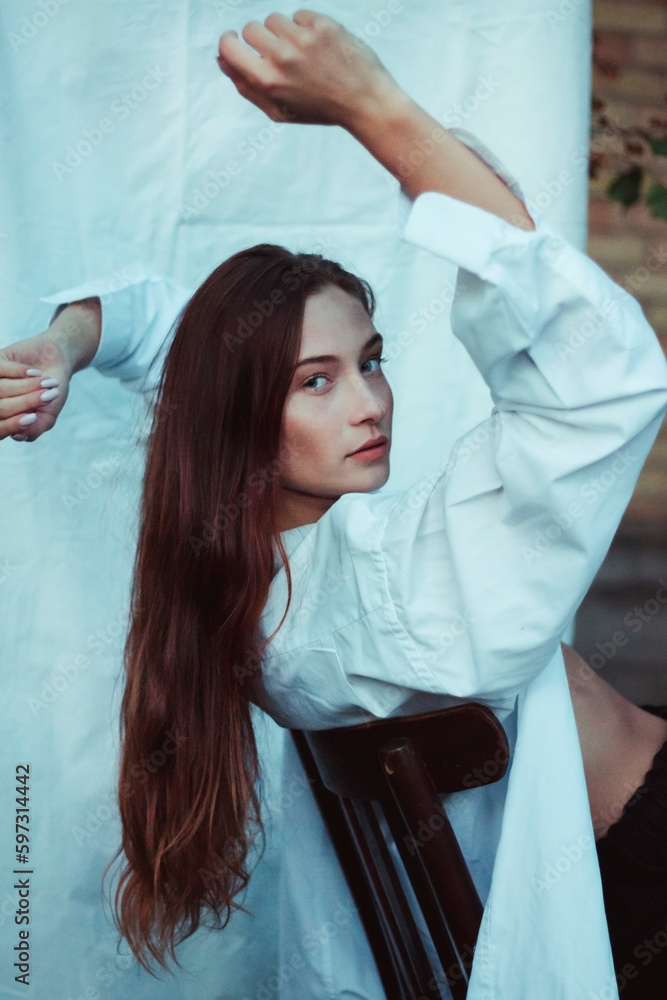 Naklejka premium Modern photo of a girl in a white shirt against a white sheet. Posing on a chair. Laconic photos of a confident woman