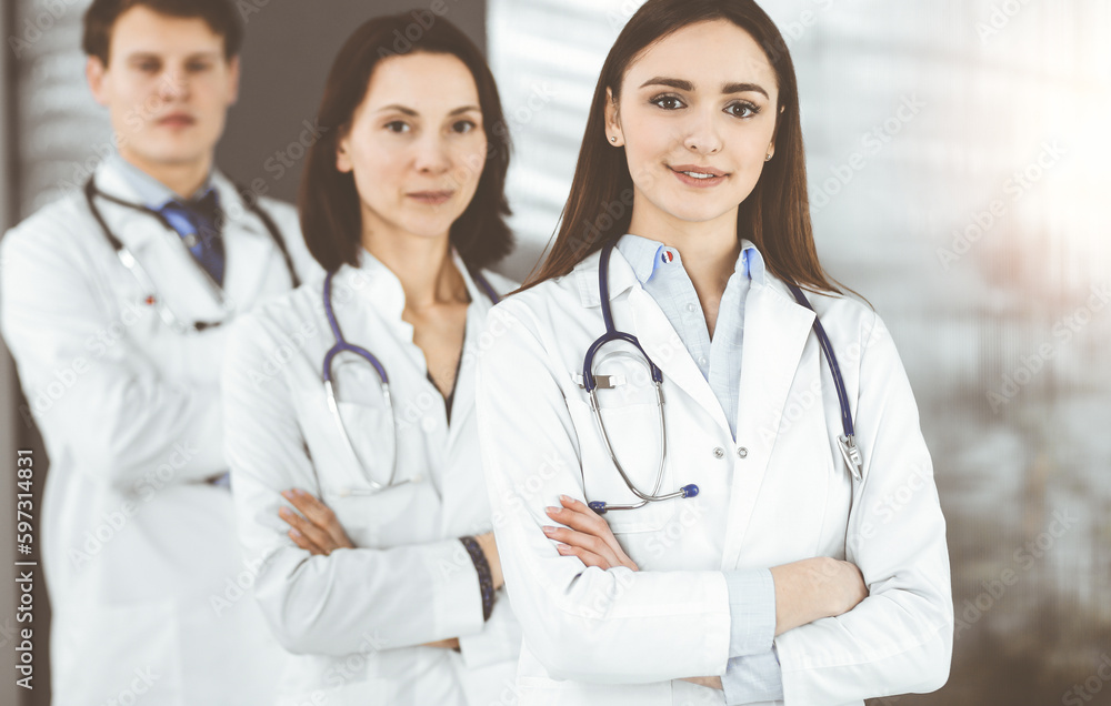 Group of young professional doctors standing as a team with arms crossed in sunny hospital. Medical help, insurance in health care, best disease treatment and medicine concept Group of young professional doctors standing as a team with arms crossed in sunny hospital. Medical help, insurance in health care, best disease treatment and medicine concept